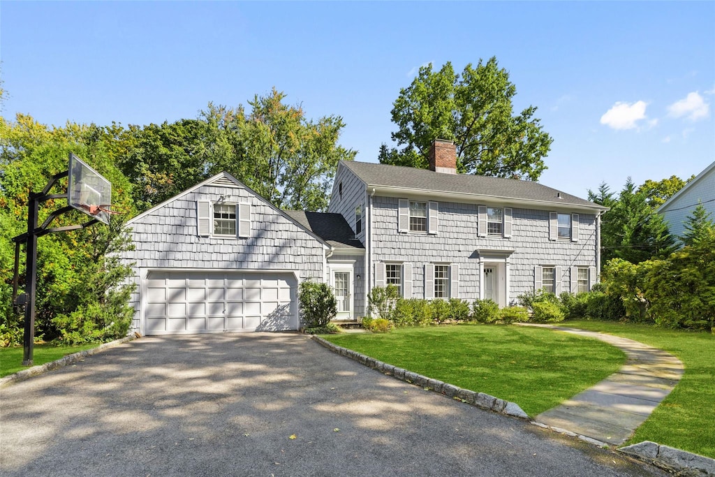 colonial house with a chimney, aphalt driveway, roof with shingles, an attached garage, and a front yard