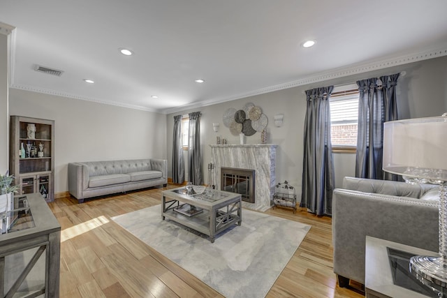 living room with a premium fireplace, ornamental molding, and light wood-type flooring