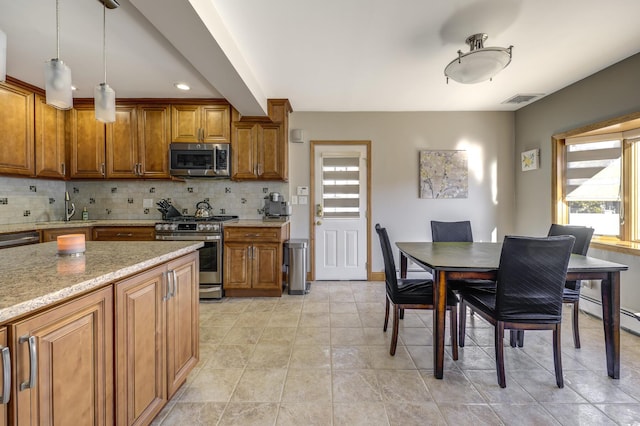 kitchen featuring appliances with stainless steel finishes, sink, decorative backsplash, hanging light fixtures, and light stone counters