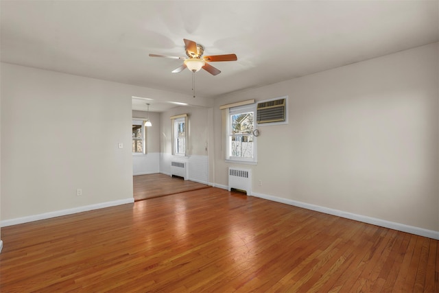 empty room featuring ceiling fan, radiator heating unit, wood-type flooring, and a wall mounted air conditioner