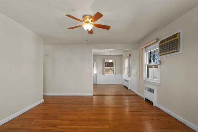 spare room with wood-type flooring, an AC wall unit, radiator, and ceiling fan