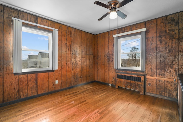 unfurnished room with hardwood / wood-style flooring, ceiling fan, wooden walls, and radiator