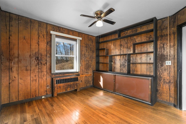 unfurnished room with ceiling fan, radiator, hardwood / wood-style floors, and wood walls