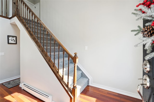 stairs with hardwood / wood-style floors, a towering ceiling, and baseboard heating