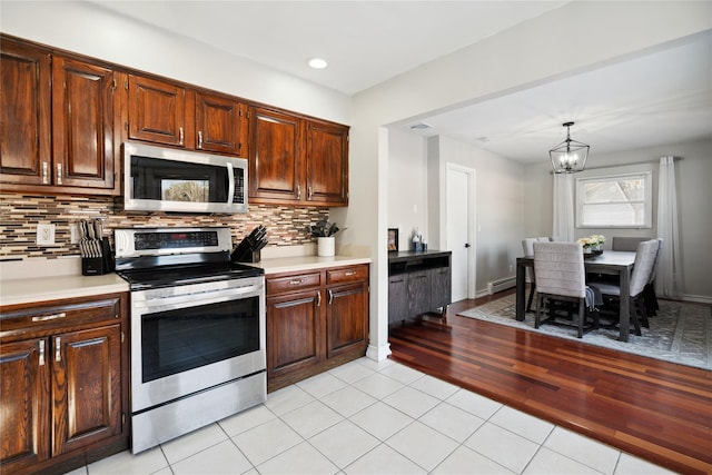 kitchen featuring tasteful backsplash, light tile patterned flooring, appliances with stainless steel finishes, and decorative light fixtures