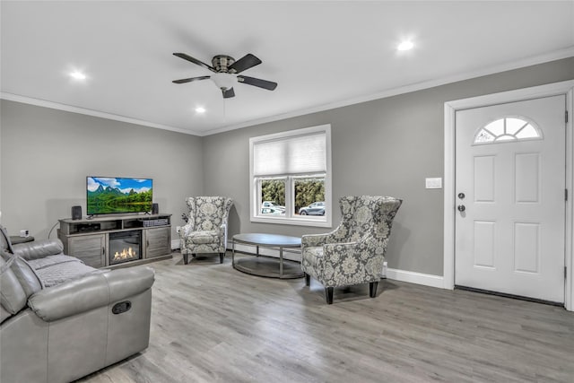 living room with ceiling fan, ornamental molding, and light wood-type flooring