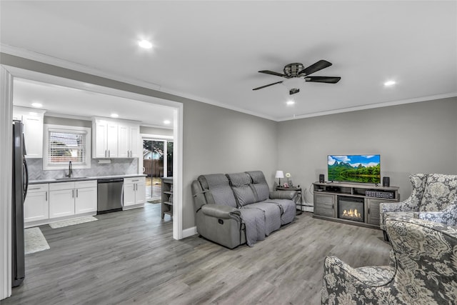 living room with a baseboard radiator, sink, ceiling fan, crown molding, and light hardwood / wood-style flooring