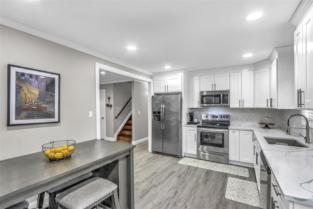 kitchen featuring sink, white cabinetry, stainless steel appliances, light stone counters, and light hardwood / wood-style floors