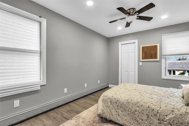 bedroom featuring wood-type flooring, a closet, ceiling fan, and baseboard heating