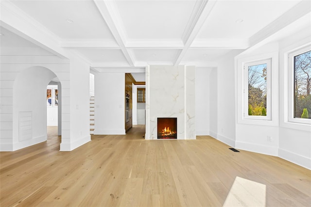 unfurnished living room featuring coffered ceiling, ornamental molding, a high end fireplace, beam ceiling, and light hardwood / wood-style floors