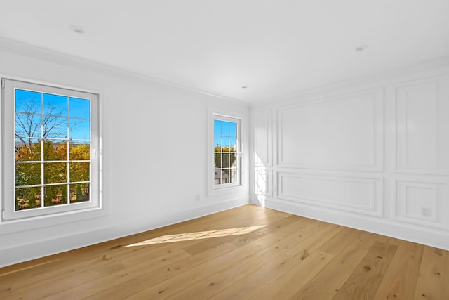 empty room with light hardwood / wood-style flooring, crown molding, and plenty of natural light