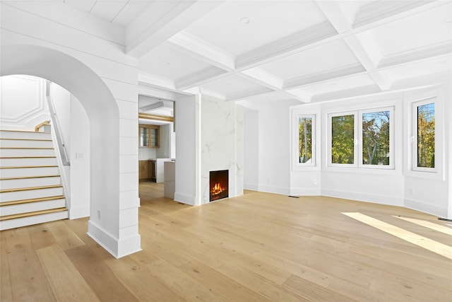 unfurnished living room featuring a fireplace, coffered ceiling, stairway, light wood finished floors, and beamed ceiling