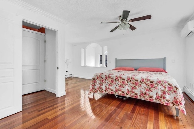 bedroom featuring a wall mounted AC, dark hardwood / wood-style flooring, ornamental molding, ceiling fan, and a textured ceiling