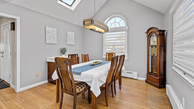 dining area with vaulted ceiling with skylight, baseboard heating, and light hardwood / wood-style flooring