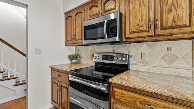 kitchen with tasteful backsplash, light stone countertops, light hardwood / wood-style floors, and appliances with stainless steel finishes