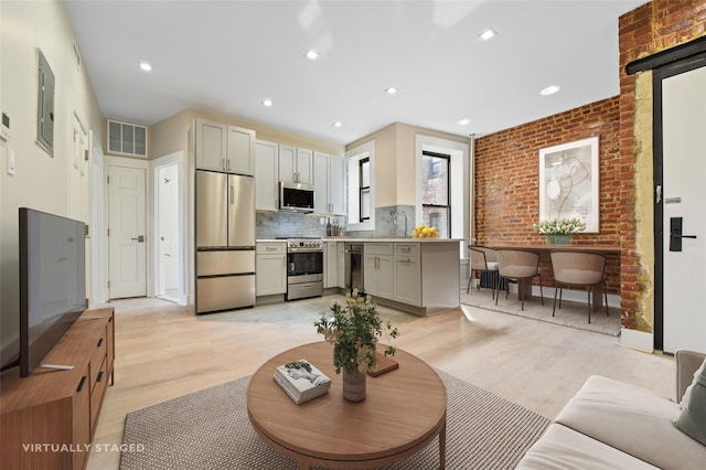 living room with sink, electric panel, brick wall, and light wood-type flooring