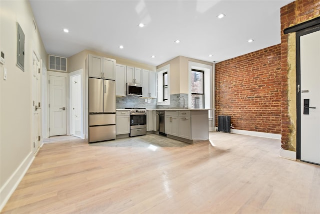 kitchen featuring stainless steel appliances, light hardwood / wood-style flooring, electric panel, brick wall, and backsplash