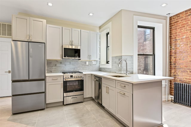 kitchen featuring sink, appliances with stainless steel finishes, radiator, brick wall, and decorative backsplash