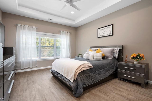 bedroom with ceiling fan, light wood-type flooring, and a tray ceiling