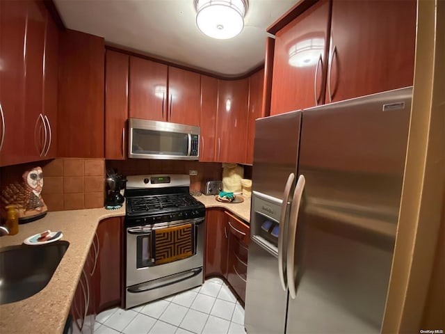 kitchen with light tile patterned floors, tasteful backsplash, light stone countertops, stainless steel appliances, and a sink