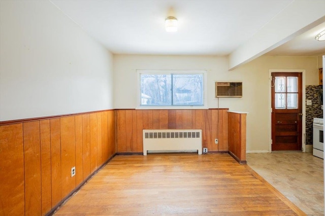 unfurnished room featuring a wall mounted air conditioner, radiator heating unit, wooden walls, and light wood-type flooring