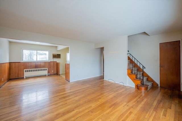 unfurnished living room with radiator heating unit, light hardwood / wood-style floors, and a wall mounted air conditioner