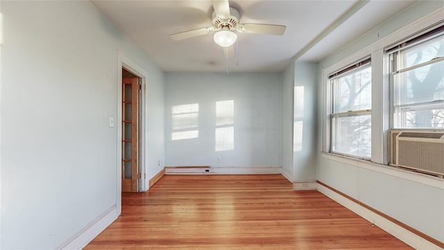 spare room featuring cooling unit, light wood-style flooring, baseboards, and a ceiling fan