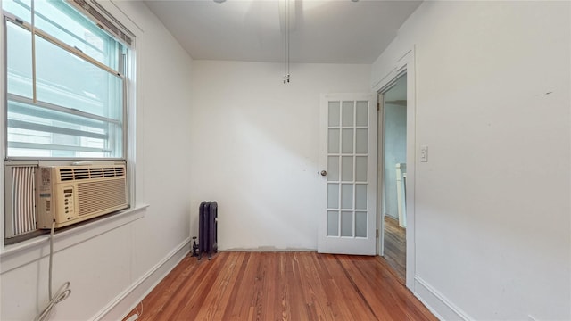 unfurnished room with cooling unit, radiator, and wood finished floors