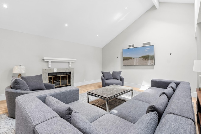 living room featuring beamed ceiling, a premium fireplace, high vaulted ceiling, and light hardwood / wood-style floors