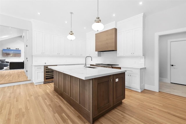 kitchen with sink, an island with sink, beverage cooler, and white cabinets