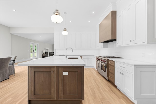 kitchen with wall chimney range hood, sink, white cabinets, decorative light fixtures, and range with two ovens