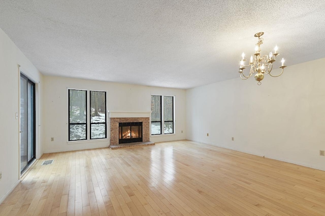 unfurnished living room with an inviting chandelier, a wealth of natural light, a fireplace, and light hardwood / wood-style floors