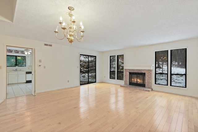 unfurnished living room featuring sink, a notable chandelier, a brick fireplace, a textured ceiling, and light hardwood / wood-style flooring