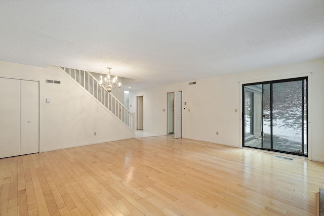 unfurnished room featuring light hardwood / wood-style floors, a textured ceiling, and a notable chandelier