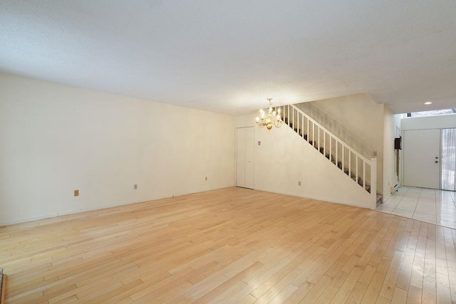 unfurnished living room featuring a chandelier, a textured ceiling, and light wood-type flooring