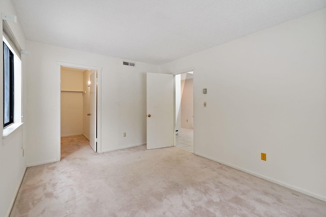 unfurnished bedroom featuring light carpet and a walk in closet