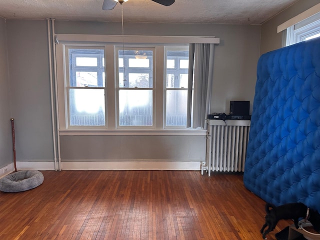 empty room featuring ceiling fan, radiator heating unit, a textured ceiling, and dark hardwood / wood-style flooring