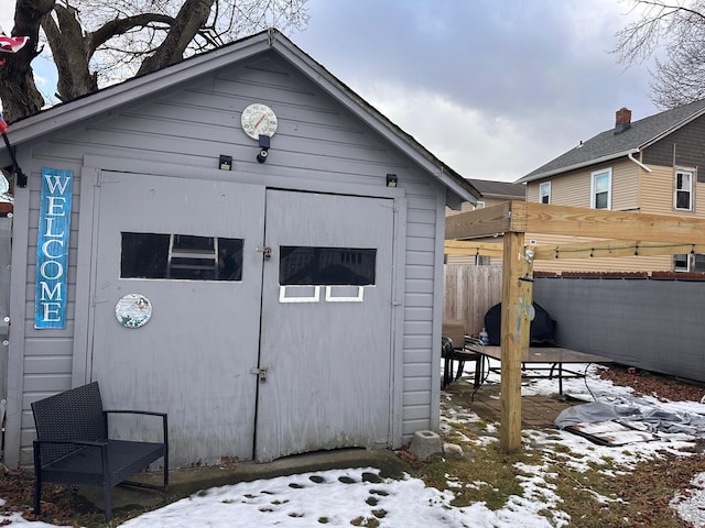 snow covered structure featuring an outdoor structure, fence, and a shed