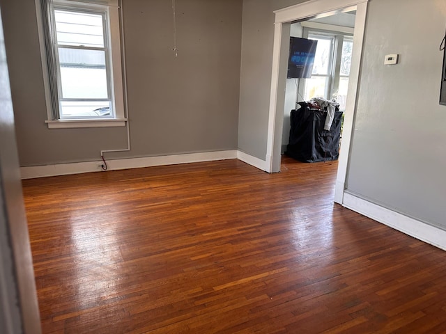 empty room featuring dark wood-style floors, baseboards, and a wealth of natural light