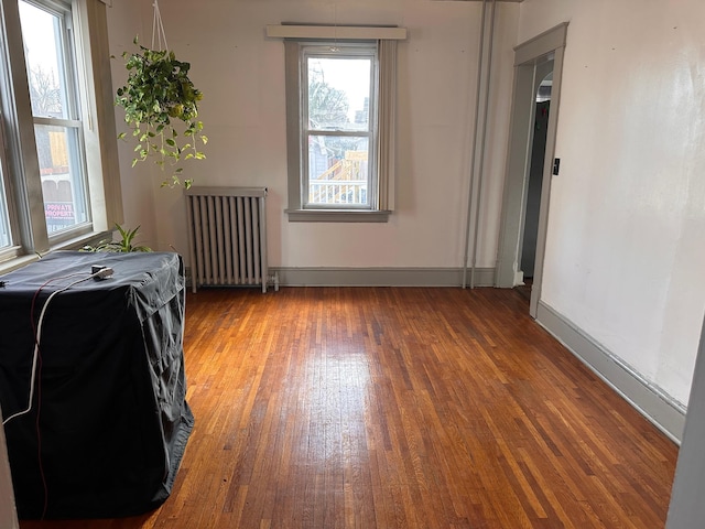 unfurnished room featuring baseboards, wood finished floors, and radiator