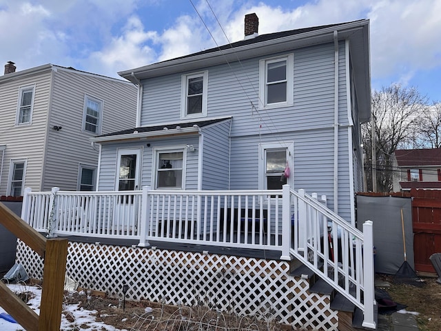 snow covered back of property featuring a deck and a chimney