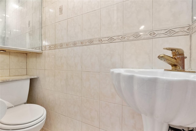 bathroom featuring toilet, tile walls, and a sink