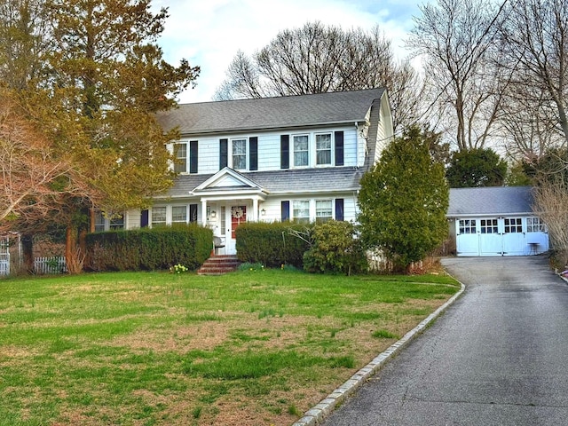 view of front of house featuring aphalt driveway, a shingled roof, an outdoor structure, and a front yard