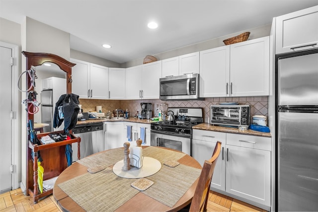 kitchen with stainless steel appliances, dark stone counters, decorative backsplash, and white cabinets