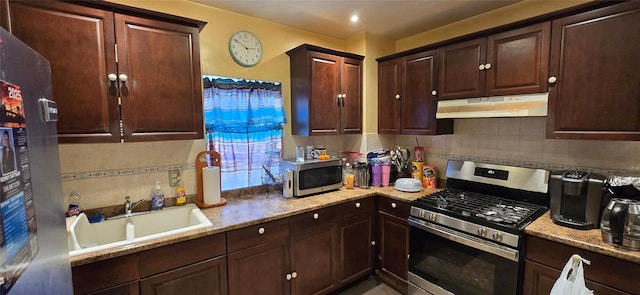 kitchen with under cabinet range hood, appliances with stainless steel finishes, tasteful backsplash, and a sink