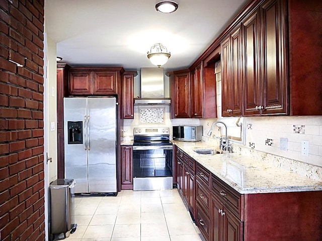 kitchen with appliances with stainless steel finishes, sink, light tile patterned floors, light stone counters, and wall chimney range hood