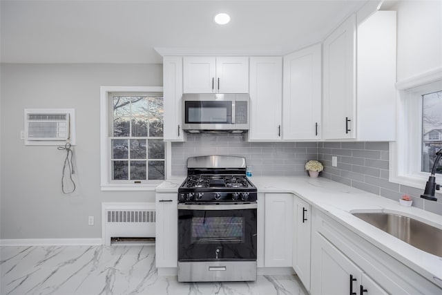 kitchen with sink, tasteful backsplash, appliances with stainless steel finishes, radiator, and white cabinets