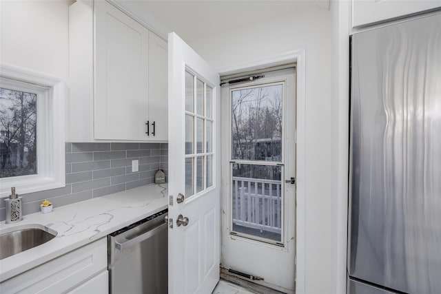 kitchen featuring white cabinetry, stainless steel appliances, light stone countertops, and decorative backsplash