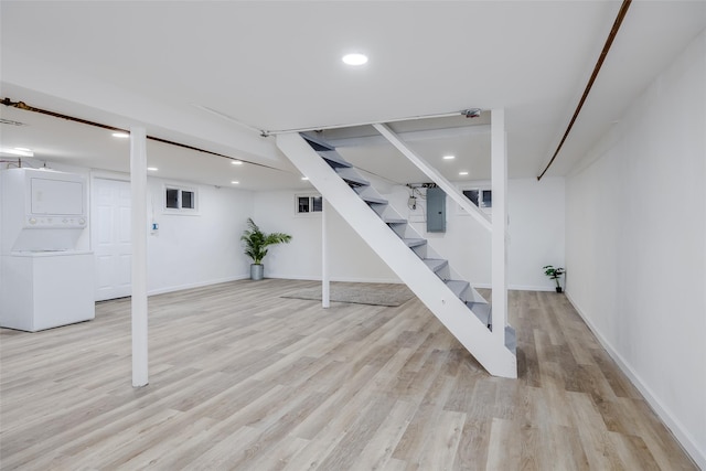 basement with stacked washer and clothes dryer, electric panel, and light wood-type flooring