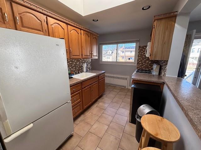 kitchen featuring radiator, tasteful backsplash, sink, white refrigerator, and light tile patterned floors